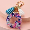 Macro shot of resin letter Q keychain with colorful stones and blue white tassels - Letter Q