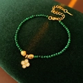 Detail eines grünen Malachit-Armbands mit goldenem Kleeblatt-Anhänger auf Samt - Grüne Blume Kleeblatt / Gold