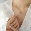 Golden M letter necklace and diamond-encrusted rings set worn on white lace top - Letter M / Gold