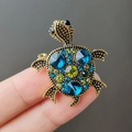 Broche de tortuga dorada vintage con cristales azules y verdes sostenido con los dedos - Azul