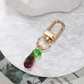 Golden keychain featuring a gradient purple glass eggplant pendant on white plate - Eggplant
