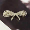Fermaglio per capelli a fiocco dorato con strass e perle bianche su sfondo scuro - Fiocco di Perle