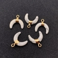 Close-up of crescent-shaped white marble stone pendants with gold bails for DIY jewelry - Howlite
