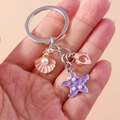 Close-up of metal keychain featuring pink shell, starfish with pearls and small conch - Purple Shell Starfish