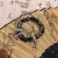 Elegant black obsidian beaded bracelet with silver Fu pendant and leaf charm over a fan - Silver/Sand Beads