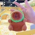 Close-up of a cute plush capybara keychain with a green hood held in hand - Frog Hat Dark Brown + Bead Chain