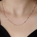Close-up of minimalist rose gold thin chain necklace with water wave texture on skin - Rose Gold