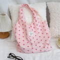 Vue détaillée du sac cabas en toile à motif cœurs roses sur un lit blanc dans un décor doux - Sac de style gilet