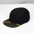 Close-up of a 5-panel camper cap with black crown and camouflage flat brim detail - Black + Camo Brim