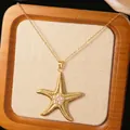 Close-up of golden starfish necklace pendant with white pearl center on a linen background - Gold Pearl Starfish Pendant Necklace