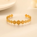 Detail of gold open bangle with embossed sun pattern charms on a soft beige background - Gold Sun Disc