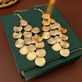 Detailed view of long gold tassel earrings with metallic sequins on a green jewelry box - Gold