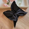 Detail of a black satin scarf scrunchie with a pink brand tag on a wooden surface - Bright Black