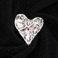 Macro shot of silver irregular lava texture heart brooch on black pleated fabric background - Silver