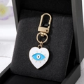Detail of white enamel heart evil eye pendant with polished gold clip on black velvet - White Heart Eyelash Eye
