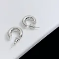 Gros plan de boucles d'oreilles créoles C en argent poli sur un support blanc élégant - Argenté
