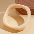 Detail eines cremigen Harzarmreifs mit Wellenkanten auf einem Holzständer - Beige
