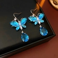 Nahaufnahme der blauen Kristall-Schmetterlings-Ohrringe mit silbernen Haken auf dunklem Grund - Ohrringhaken / Blau