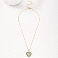 Collier cœur doré orné de cristaux verts et blancs sur une surface en pierre texturée - Zircone Vert Émeraude