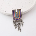 Detail of a U-shaped colorful woven brooch featuring vibrant tassels and sparkly rhinestones - Letter U