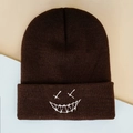 Detailed view of dark brown knitted beanie with white embroidered grimace and wide brim - One Size / Coffee