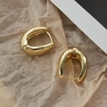 Makroaufnahme von polierten goldfarbenen U-Ohrringen auf strukturiertem Papierhintergrund - Gold