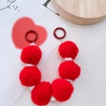 Detail of red plush ball and silver bead phone charm with heart card on white surface - Red