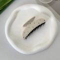 Detalle de pinza para el pelo beige de acetato con pedrería de colores en plato blanco - Pinza de diseño de orejas con dientes negros / Beige