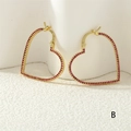 Detailaufnahme der vergoldeten Herz-Ohrringe mit roten Kristallen in Pavé-Fassung - Gold/Roter Zirkonia