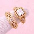 Detalle de anillos bañados en oro con circonitas cuadradas y redondas sobre fondo rosa - Estilo de Gema Cuadrada Turquesa