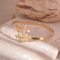 Macro-opname van gouden bladvormige manchetarmband met wit email op stenen basis - Gouden Blad Open Manchet Armband