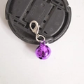 Macro shot of a purple metal bell pendant with a silver lobster clasp on a black cap - Purple