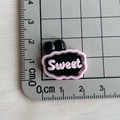 Gros plan d'une breloque Sweet en résine rose et noire avec règle de mesure sur tapis - Base Noire SWEET Rose