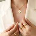 Goldene Halskette mit weißem Muschel-P-Anhänger und geschichtetem Ring-Set am Modell - Buchstabe P (RP014)