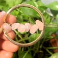 Hand holding golden round hair clip with raw rose quartz crystals on green background - Gold Circle Rose Quartz Chips