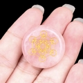 Pink quartz crystal disc with golden Flower of Life engraving held in hand - Rose Quartz