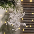 Dettaglio di un ornamento a forma di unicorno in acrilico appeso a un ramo di albero innevato - Ciondolo Unicorno Trasparente