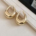 Macro detail of polished golden teardrop earrings on a beige velvet background - Gold Water Drop