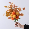 Artificial orange eucalyptus and chrysanthemum bouquet held against a plain white backdrop - Orange