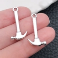 Miniature silver hammer alloy pendants for DIY keychains and necklaces shown on fingertips - 13x25mm 1.2g