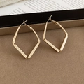 Macro detail of geometric rhombus drop earrings in polished gold metal on a display stand - Gold - Small