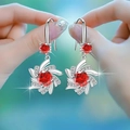 Hand holding silver flower-shaped earrings with a red gemstone center and clear crystals - Red Diamond Snowflake Earrings Led-76