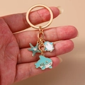 Llavero dorado con dijes de esmalte de tiburón, estrella de mar y raya sobre fondo - Estilo Estrella de Mar Tiburón / Ballena