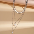 Gros plan d'un collier multicouche argenté avec des pendentifs en perles d'imitation - Argenté