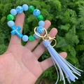 Beaded keychain bracelet with blue marble beads, Jesus cross, and tassel in outdoor view - Blue