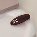 Detail shot of a dark brown oval hair clip with golden bow on a white ceramic plate - Brown
