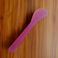 Purple silicone face mask spatula with a flat head and ergonomic handle on wood background - Transparent Pink