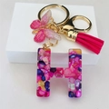 Macro shot of resin letter H keychain with colorful stones, pink butterfly and tassel - Rose Red Butterfly Tassel Clip / Letter H
