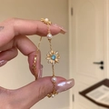 Close-up detail of a gold-tone daisy charm bracelet featuring white pearls and blue zircons - Gold
