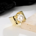 Detail van brede gouden ring met grote ronde parel en gehamerde textuur op beige steen - Verstelbaar Open / Goud
